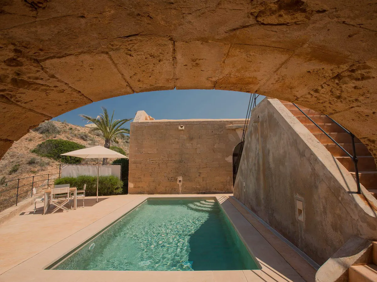 A carved stone archway frames a saltwater pool in turquoise, set within fortified walls overlooking the coast