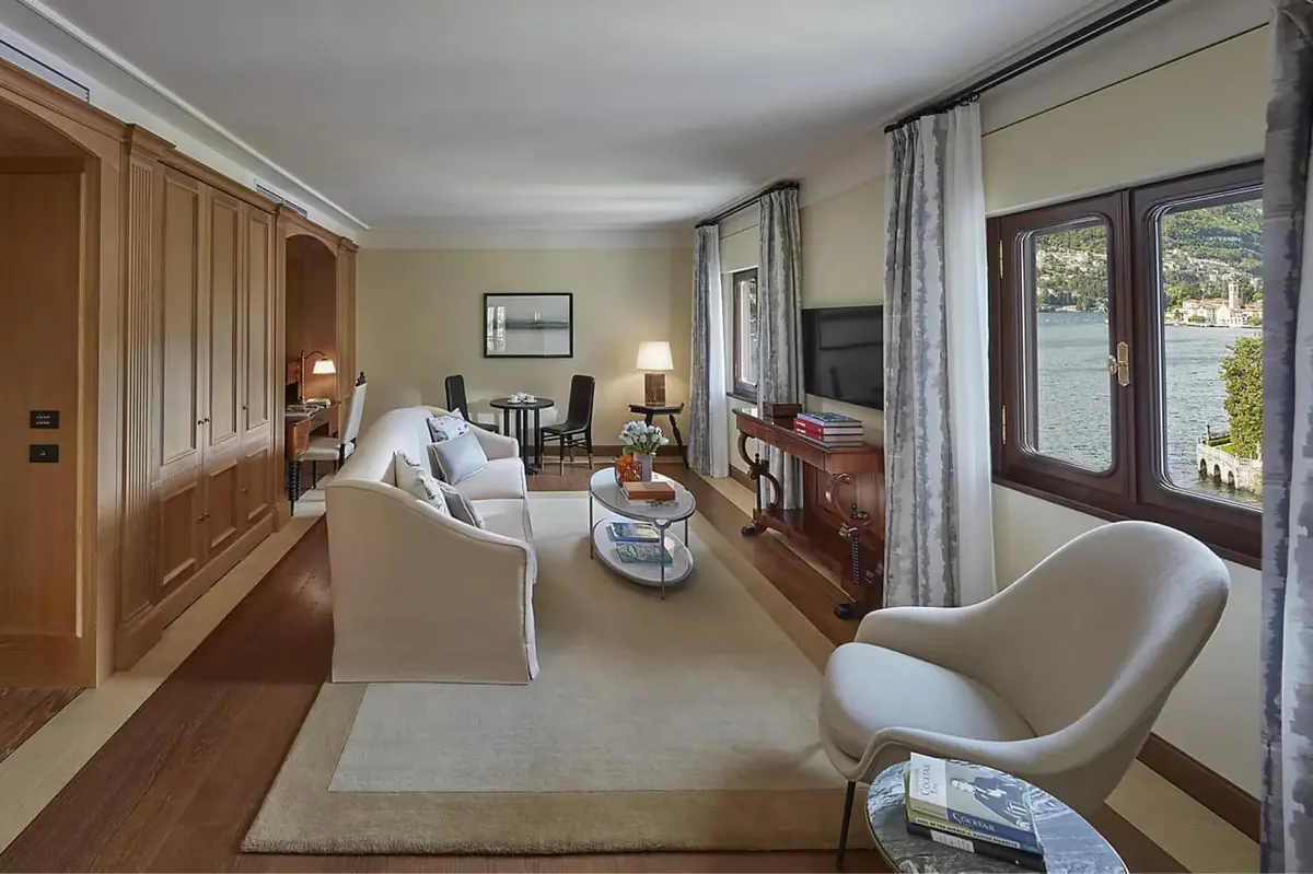 Suite with light furnishings, multiple seating zones, and views across lake to mountains