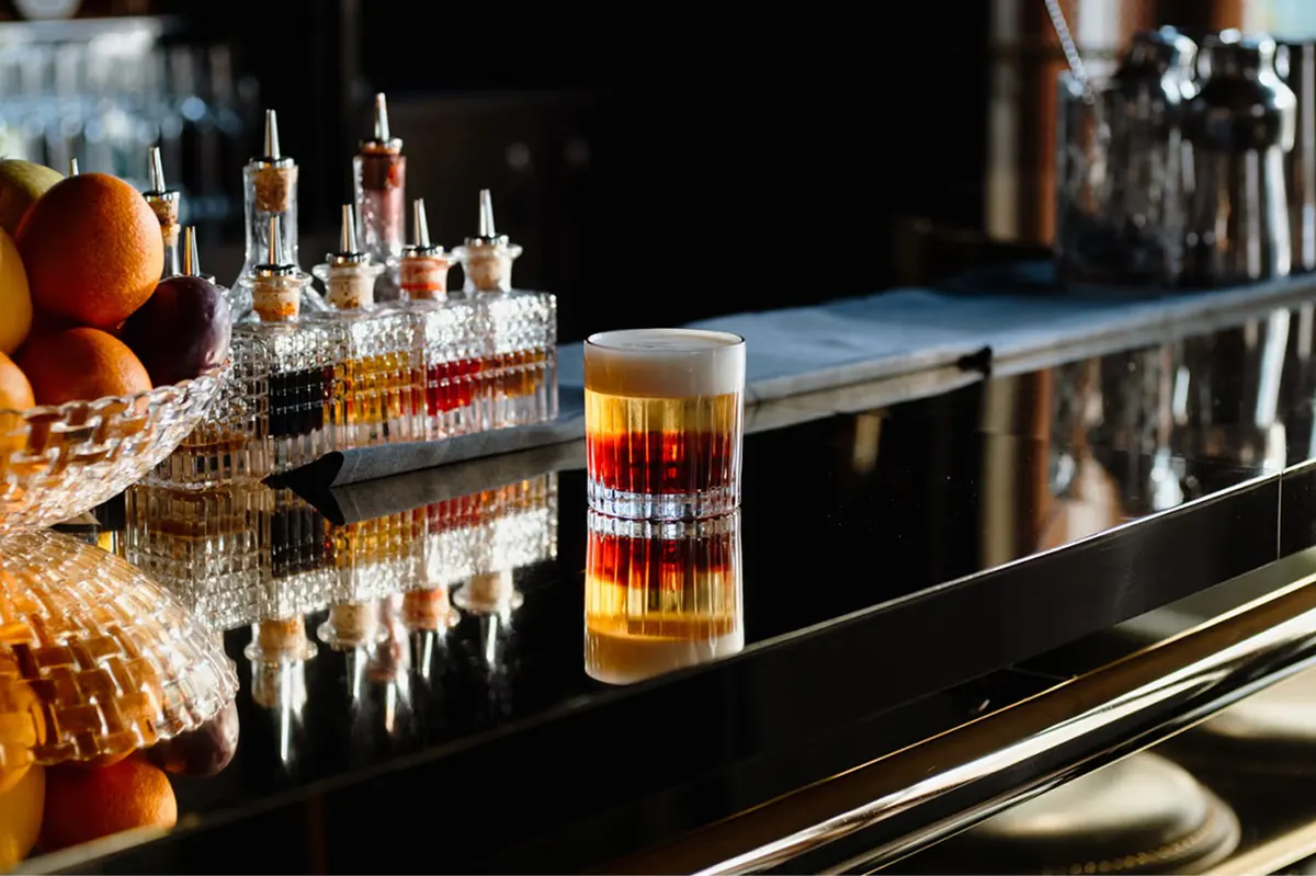 Cocktail bar with dark surface, bottles, and single glass with spirits