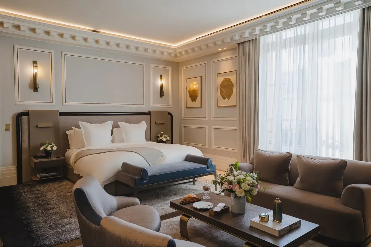 A bedroom with white and gold ceiling details, dark upholstered headboard, and window with sheer curtains
