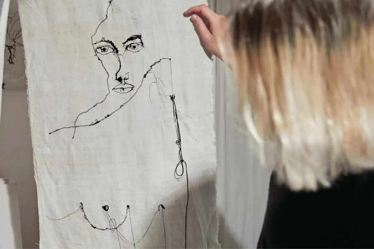 Artist sketching on linen fabric, creating linear portrait drawing with pen