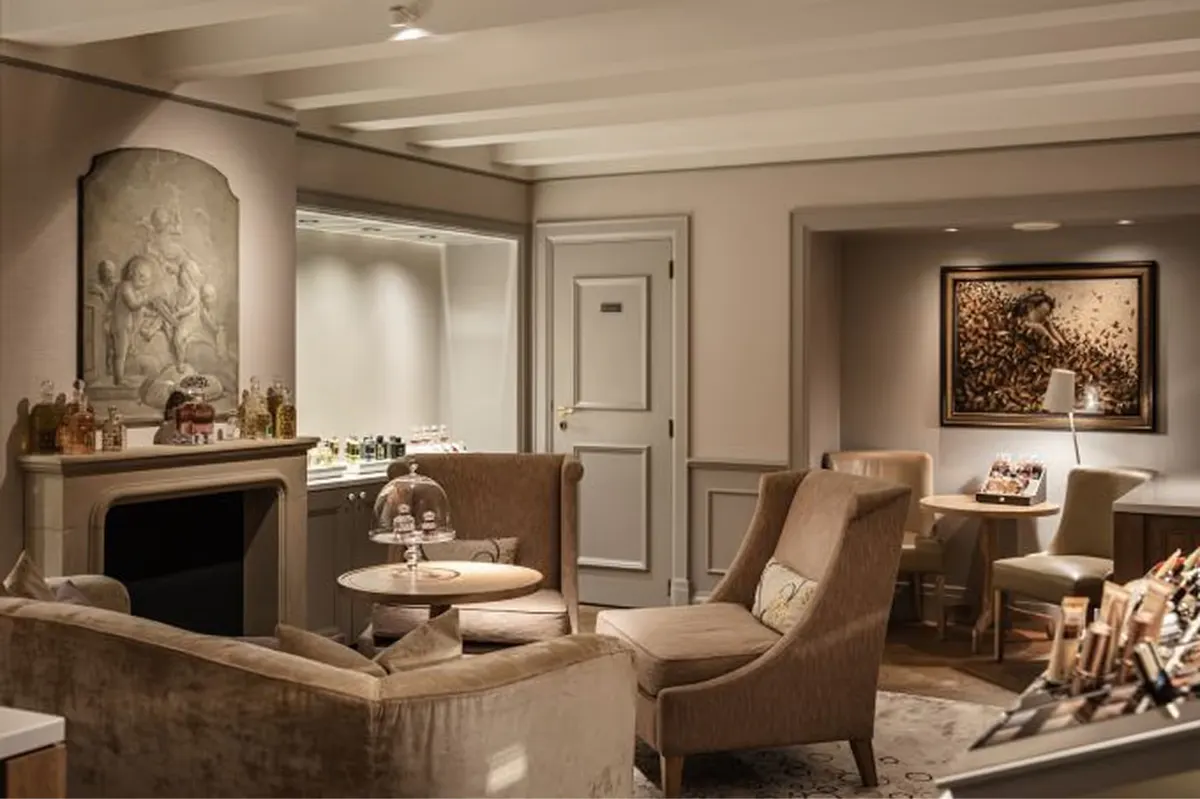 A spa lounge with cream armchairs, a marble fireplace surround, and framed botanical artworks