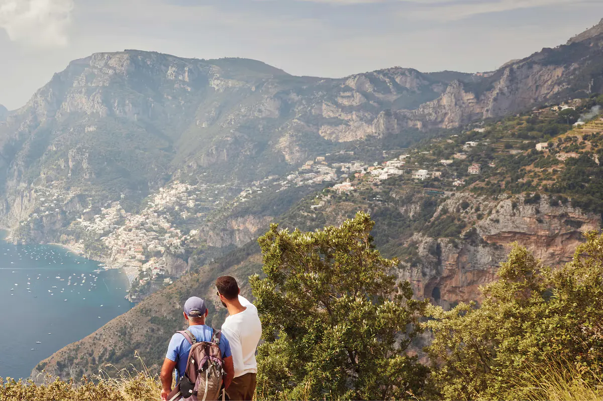Hikers with backpacks viewing terraced coast from mountain ridge overlooking villages and blue sea
