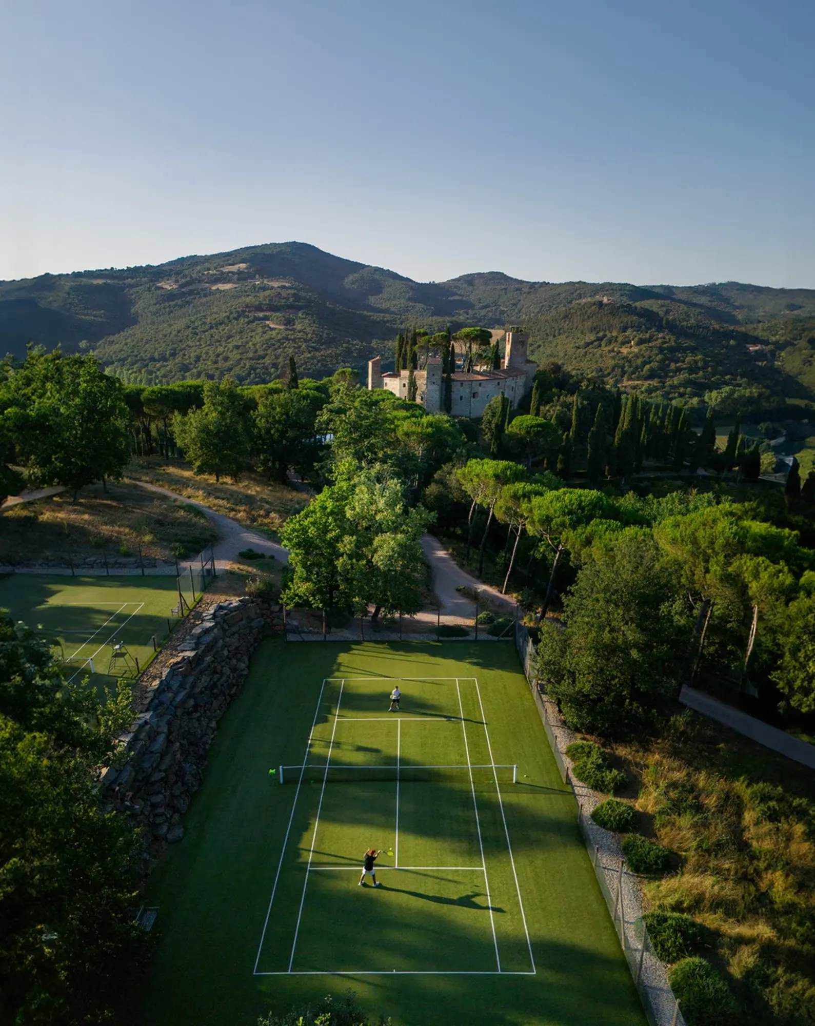 A grass tennis court below a hilltop castle in the Umbrian hills