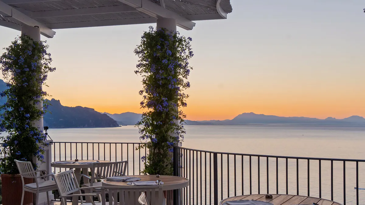 Waterfront terrace at sunset with ivy-wrapped columns framing coastal vista