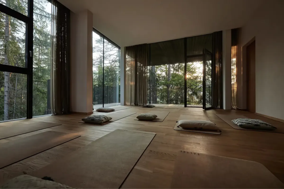Yoga and meditation studio with wood floor, cushions, and forest views through windows