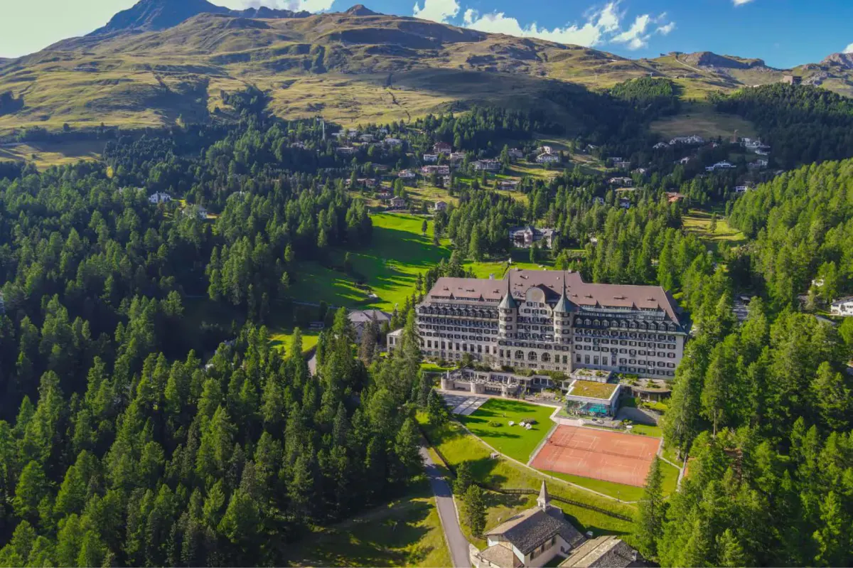 The hotel with surrounding forest and mountains, viewed from a distant elevated vantage point
