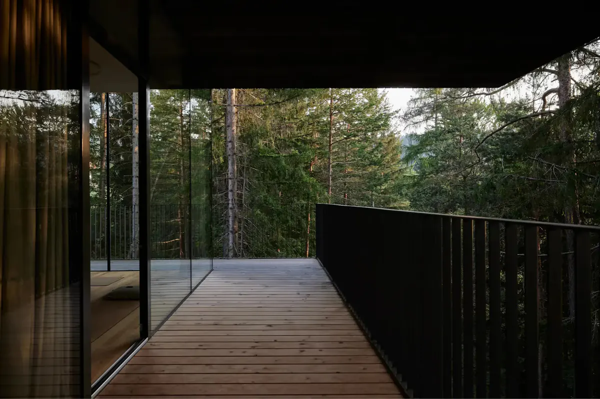 Wooden deck with glass railing overlooking forested mountainous terrain