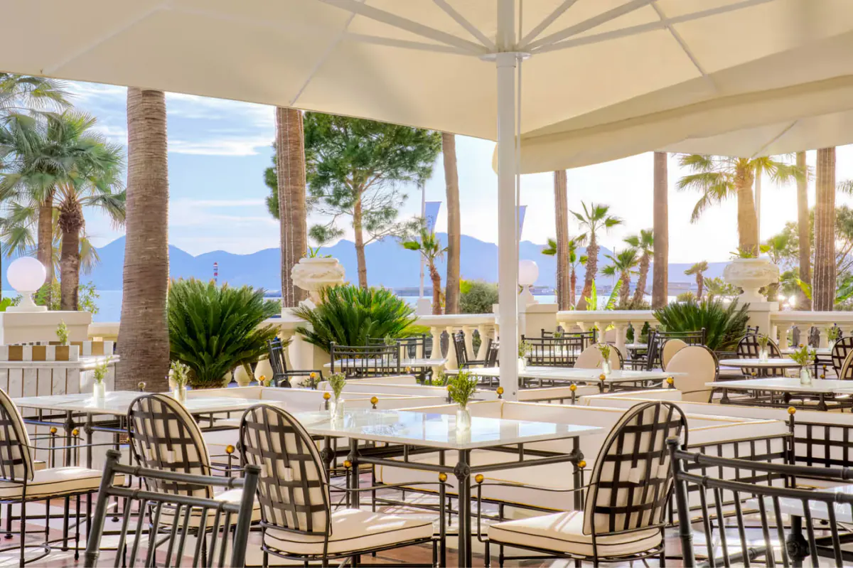 Terrace restaurant under white umbrellas with woven dining chairs and Mediterranean views