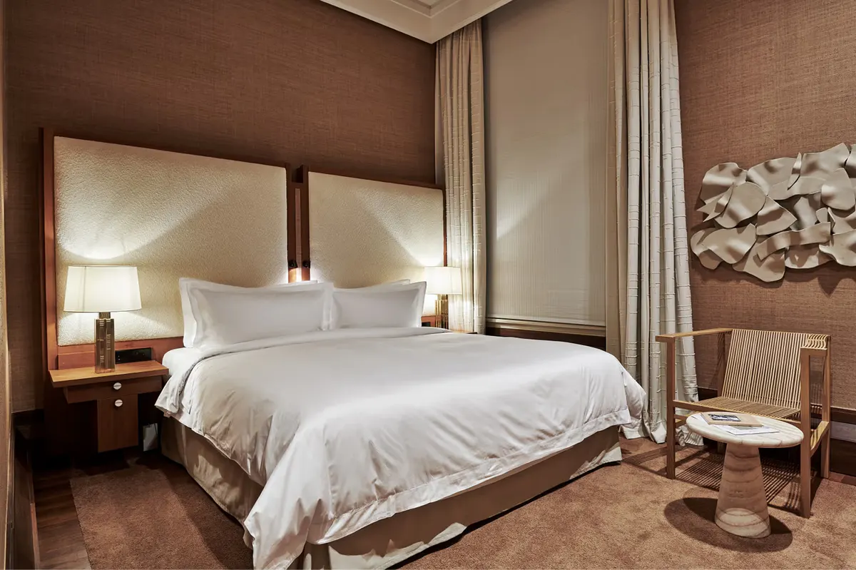 Suite bedroom with taupe upholstered walls, white bedding, and modern seating nook