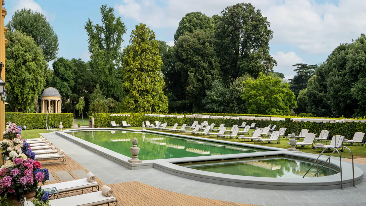 Resort pool surrounded by manicured gardens with geometric hedgerow patterns and mature shade trees