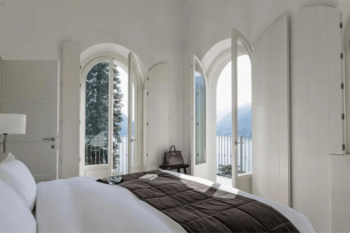 Bedroom with arched windows overlooking the lake and pale bedding with dark accent