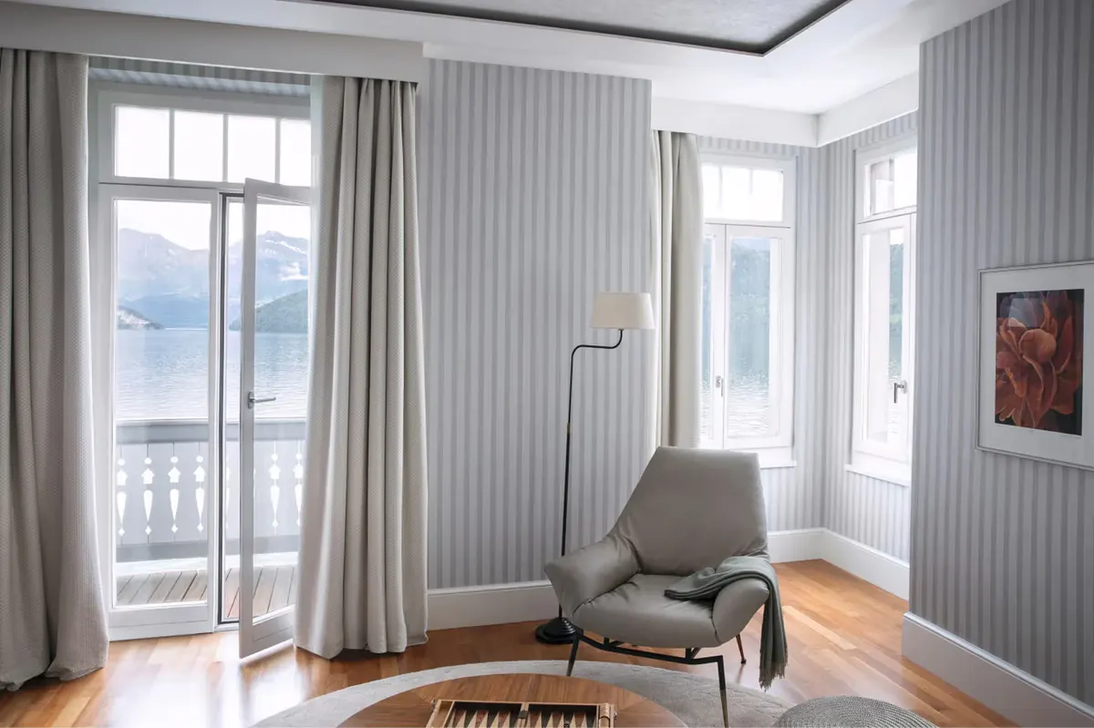 Bedroom corner with floor-to-ceiling windows, pale walls, lounge chair, and lake view