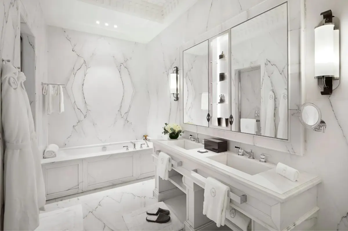 A marble bathroom with white tub, double vanity, and traditional sconce lighting
