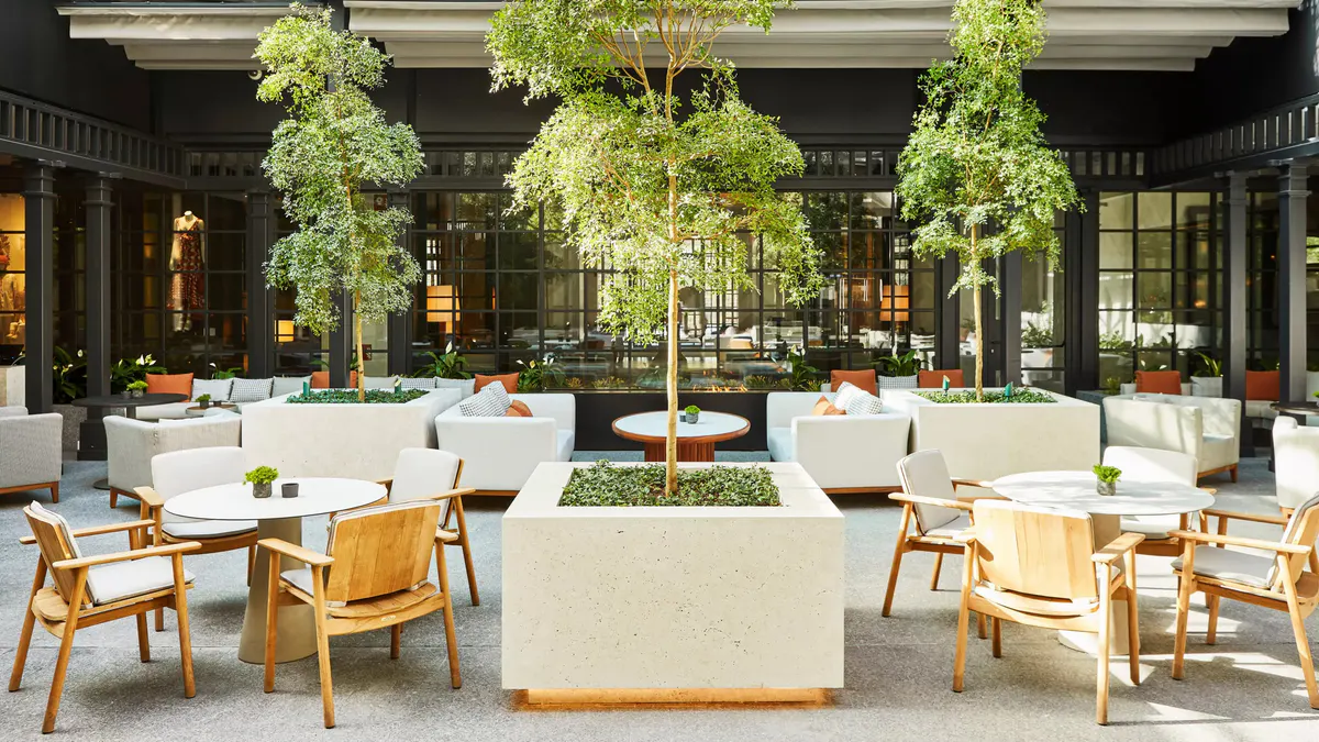 The hotel courtyard with lush hanging trees, white marble seating, and wooden chairs