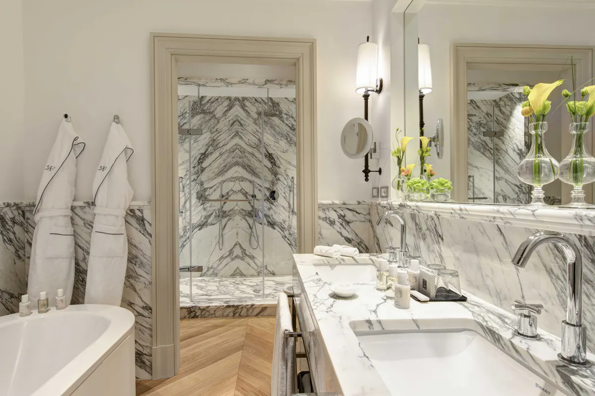 Marble bathroom with dual sinks, decorative panels, and white fixtures