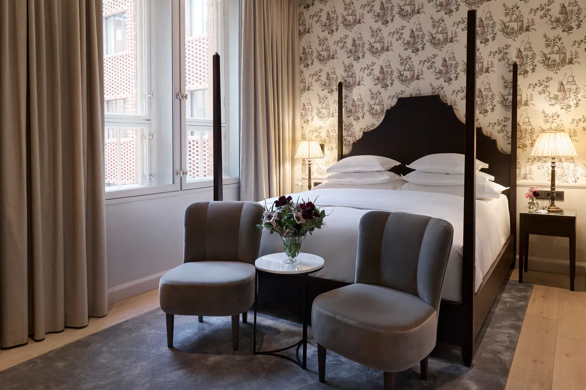 Suite with patterned wallpaper, four-poster bed, and lounge seating area
