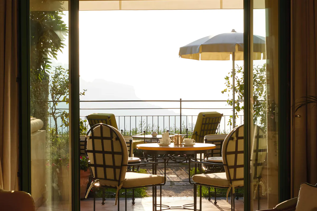 Terrace view to sea framed by open wood doors, round table with yellow umbrella, wicker chairs in afternoon light