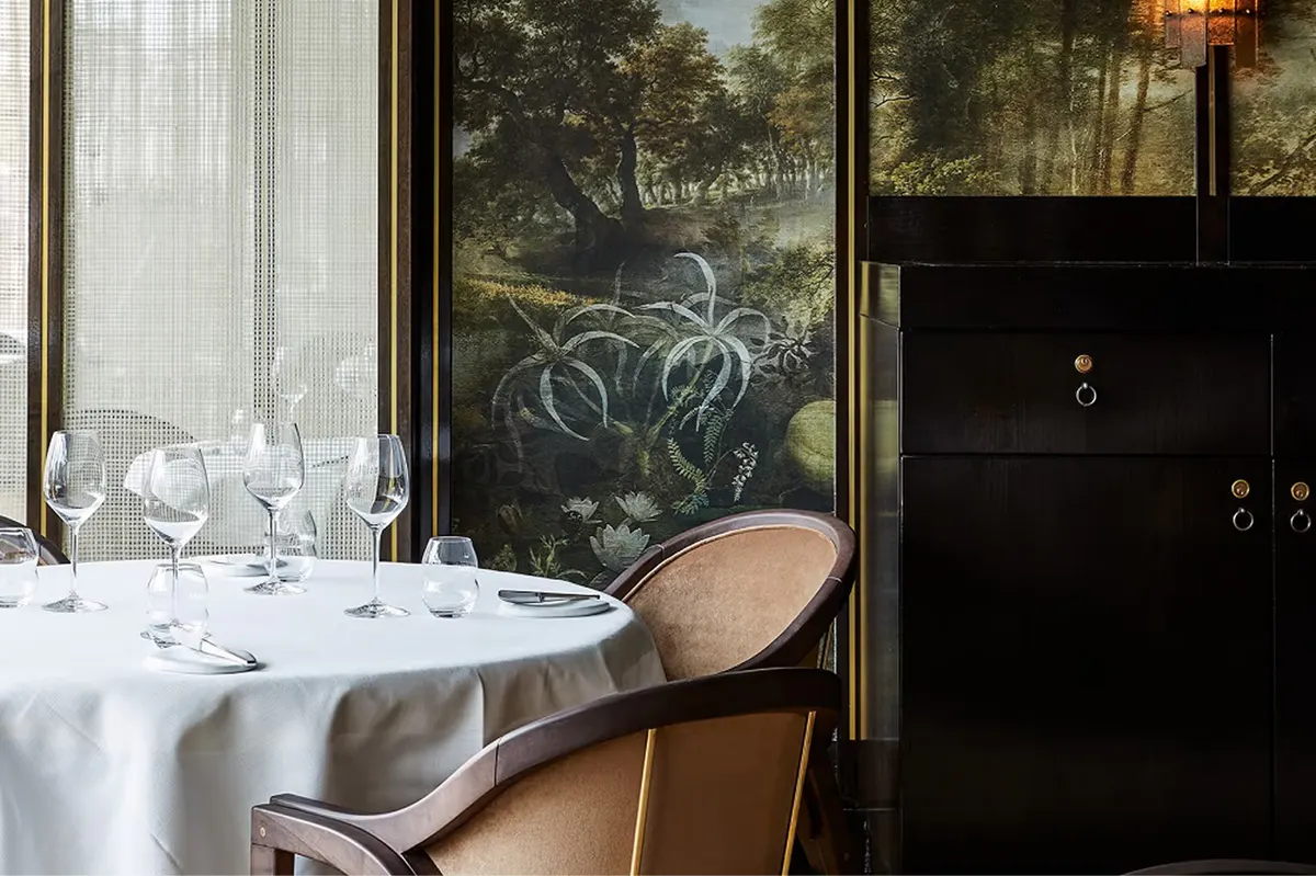 Fine dining room with white tablecloths, large windows overlooking gardens, and formal place settings