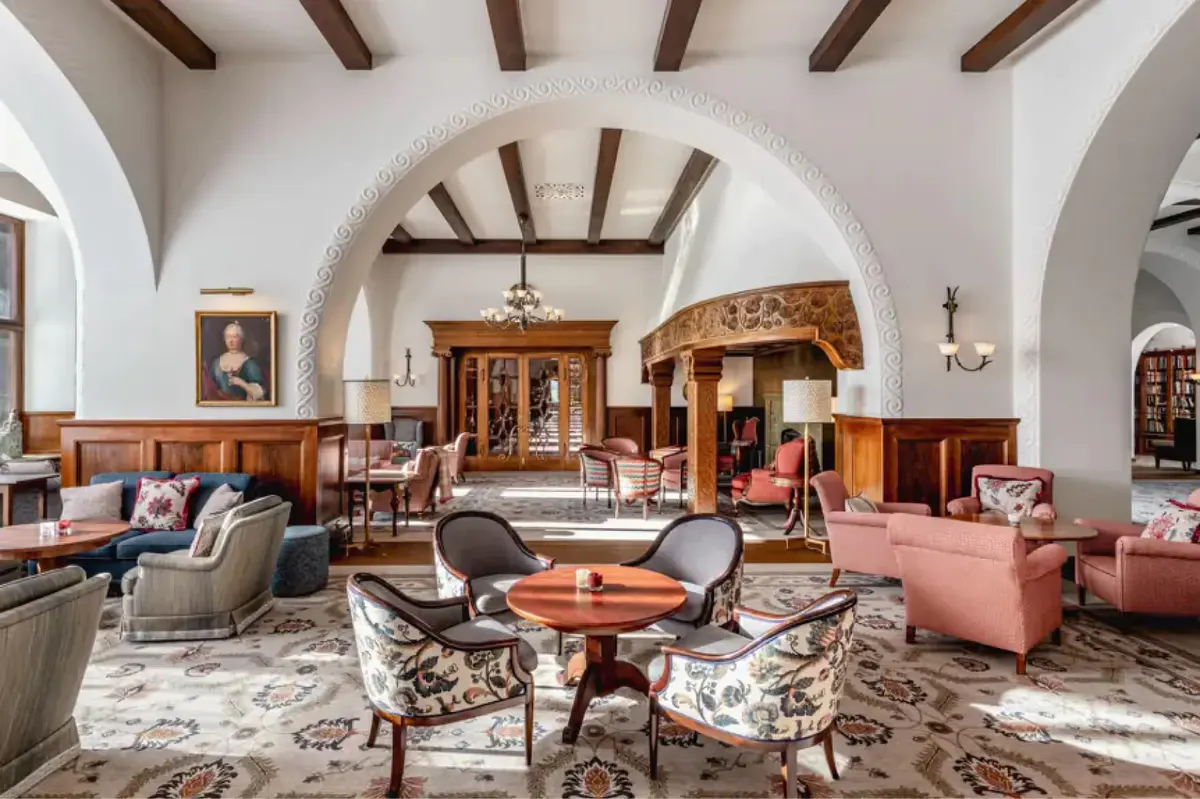 A grand interior lounge with arched ceilings, wooden beams, ornate furnishings, and classical paintings