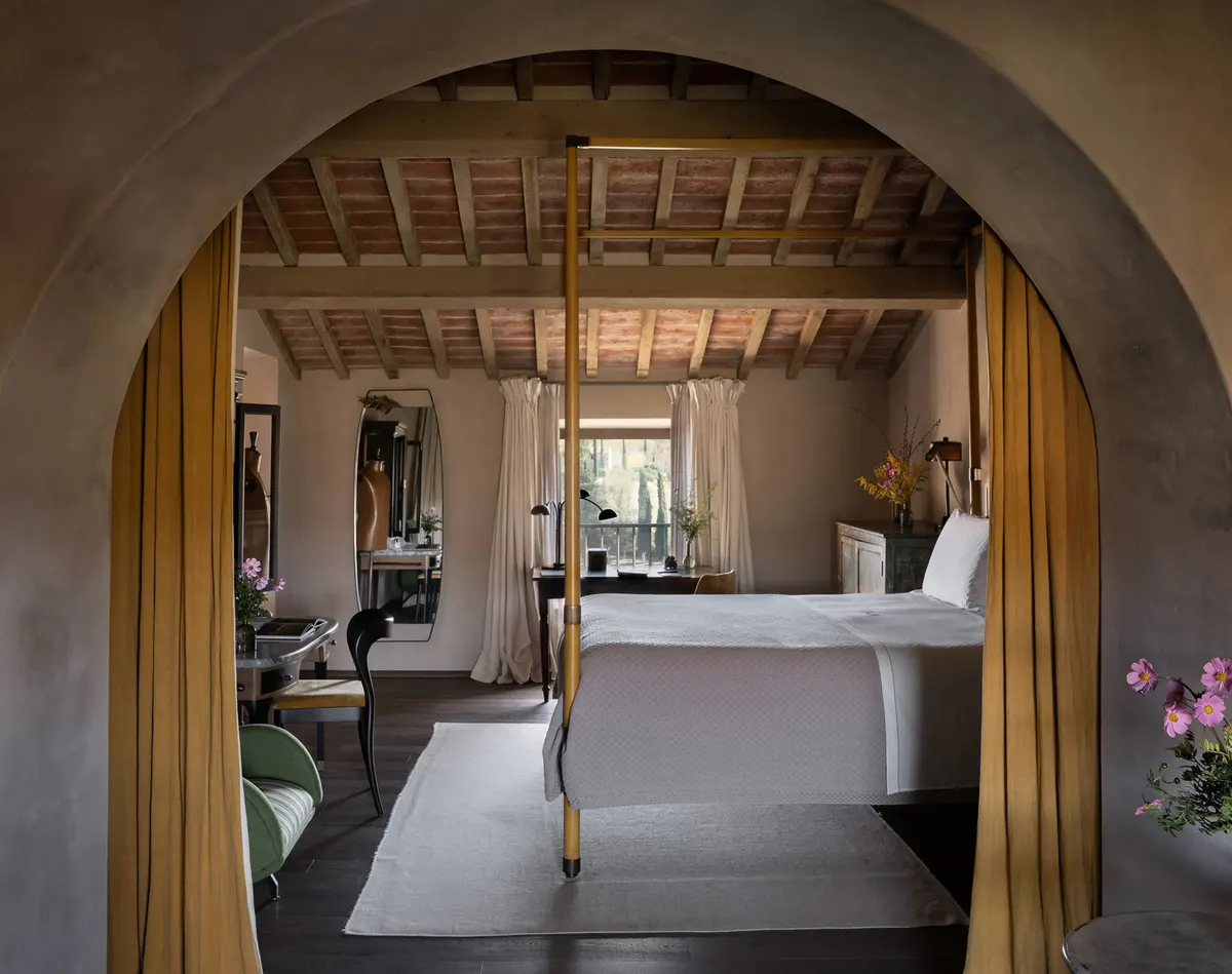 A canopy bed glimpsed through a stone archway, mustard drapes framing the timber beamed bedroom beyond