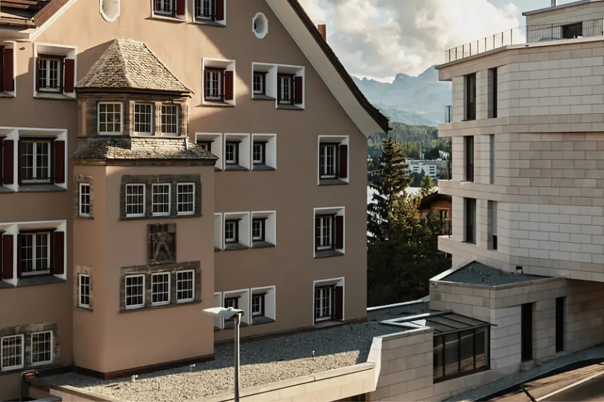 Historic stone buildings with mountains in the distance and alpine meadow below