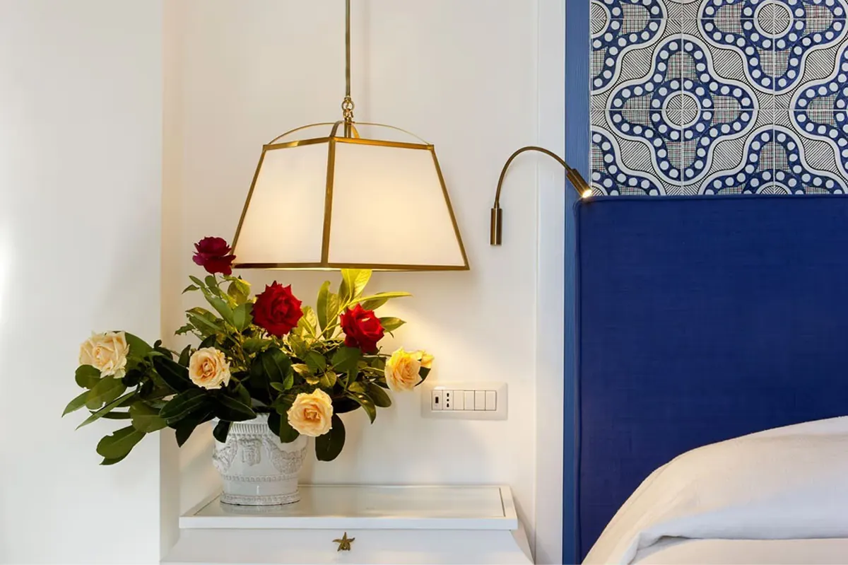 Bedside table with golden hanging pendant lamp above fresh flower arrangement in vase