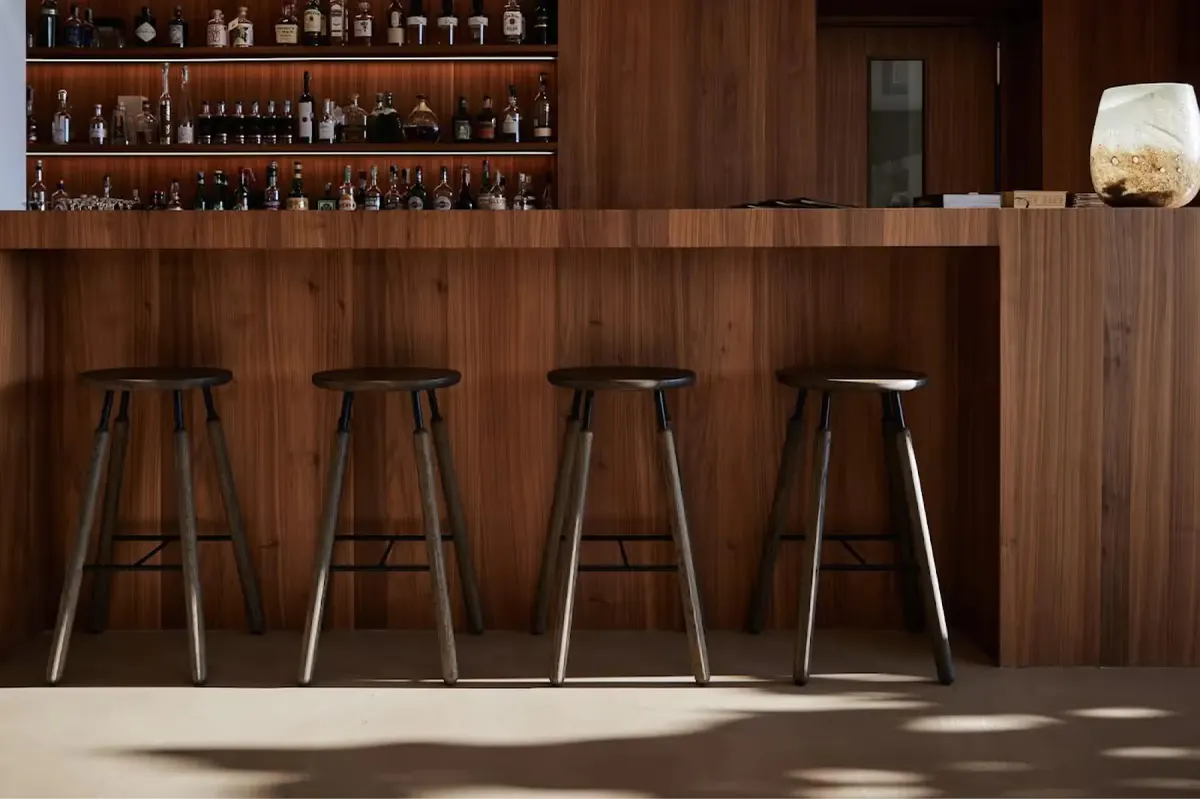 Restaurant bar counter in dark wood with bottled spirits on shelves behind and bar stools