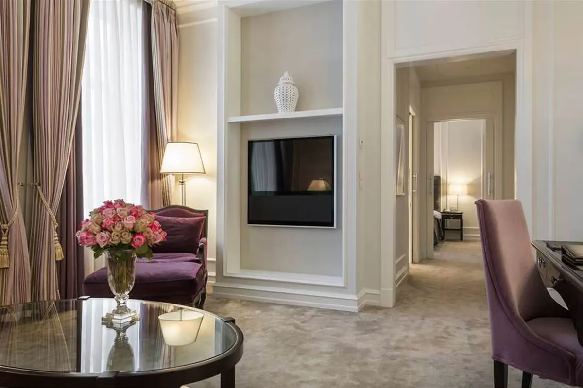 Suite sitting area with fireplace, burgundy chair, and cream furnishings