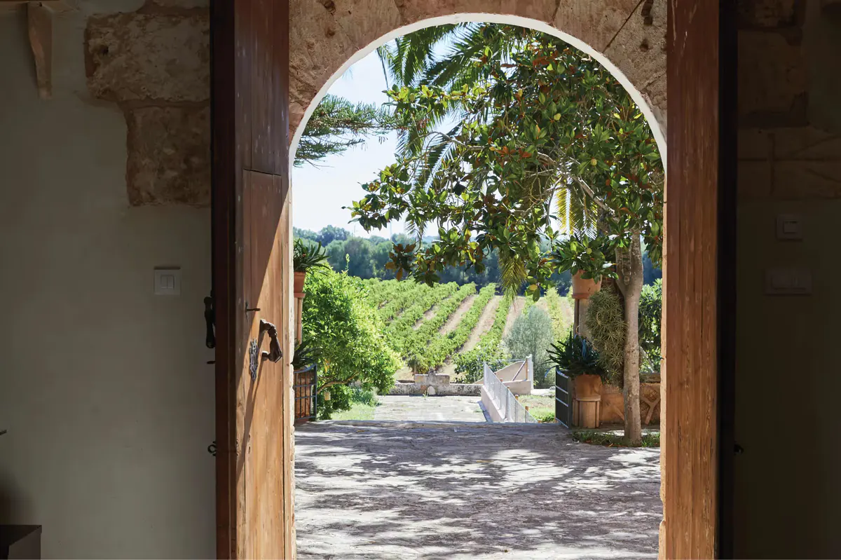 Arched wooden doorway framing a courtyard with cypress trees and mountain view