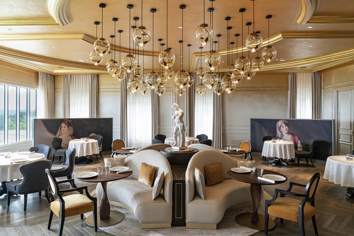 Sophisticated dining room with gold ceiling details, multiple chandeliers, and deep burgundy seating