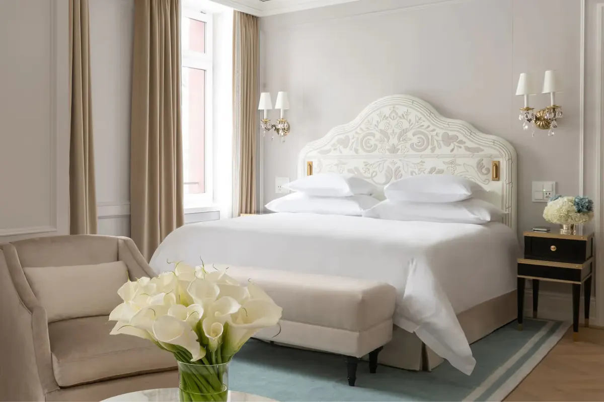 Bedroom with ornate white headboard, upholstered armchair, and fresh flowers