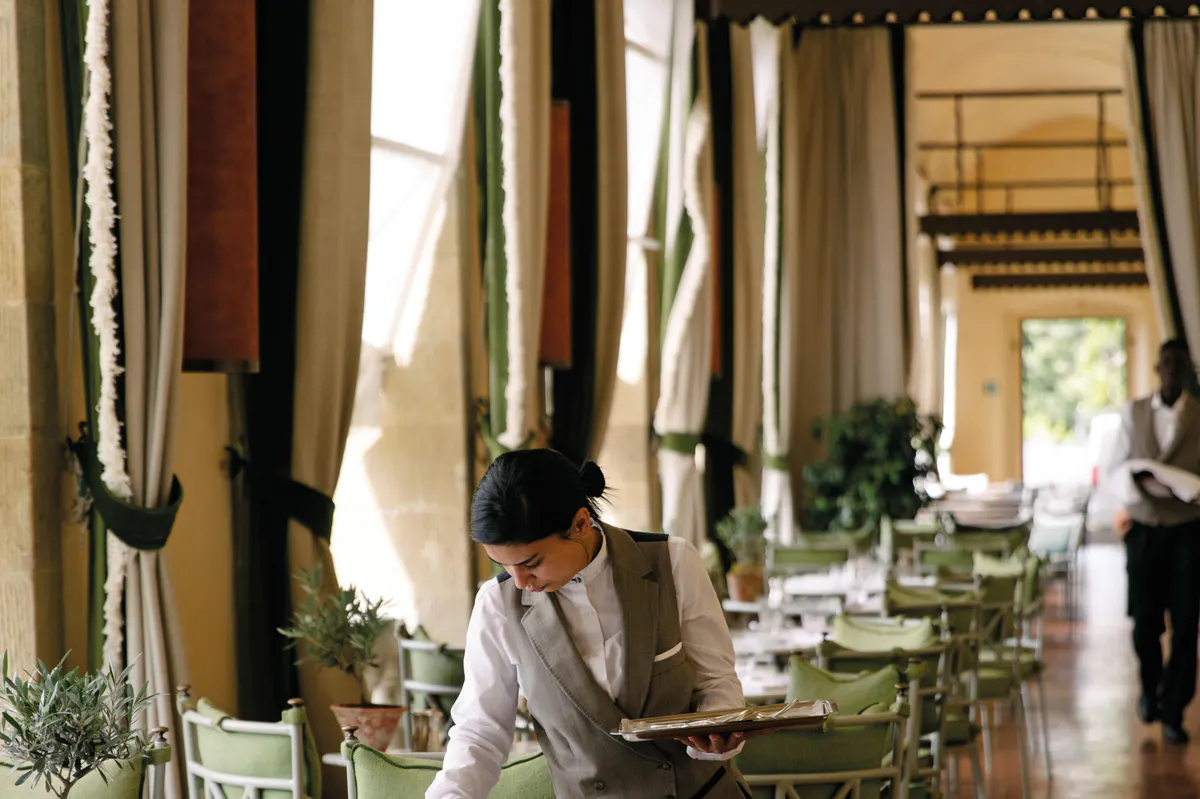 A server in white shirt working in a dining room with tall columns and draped fabric
