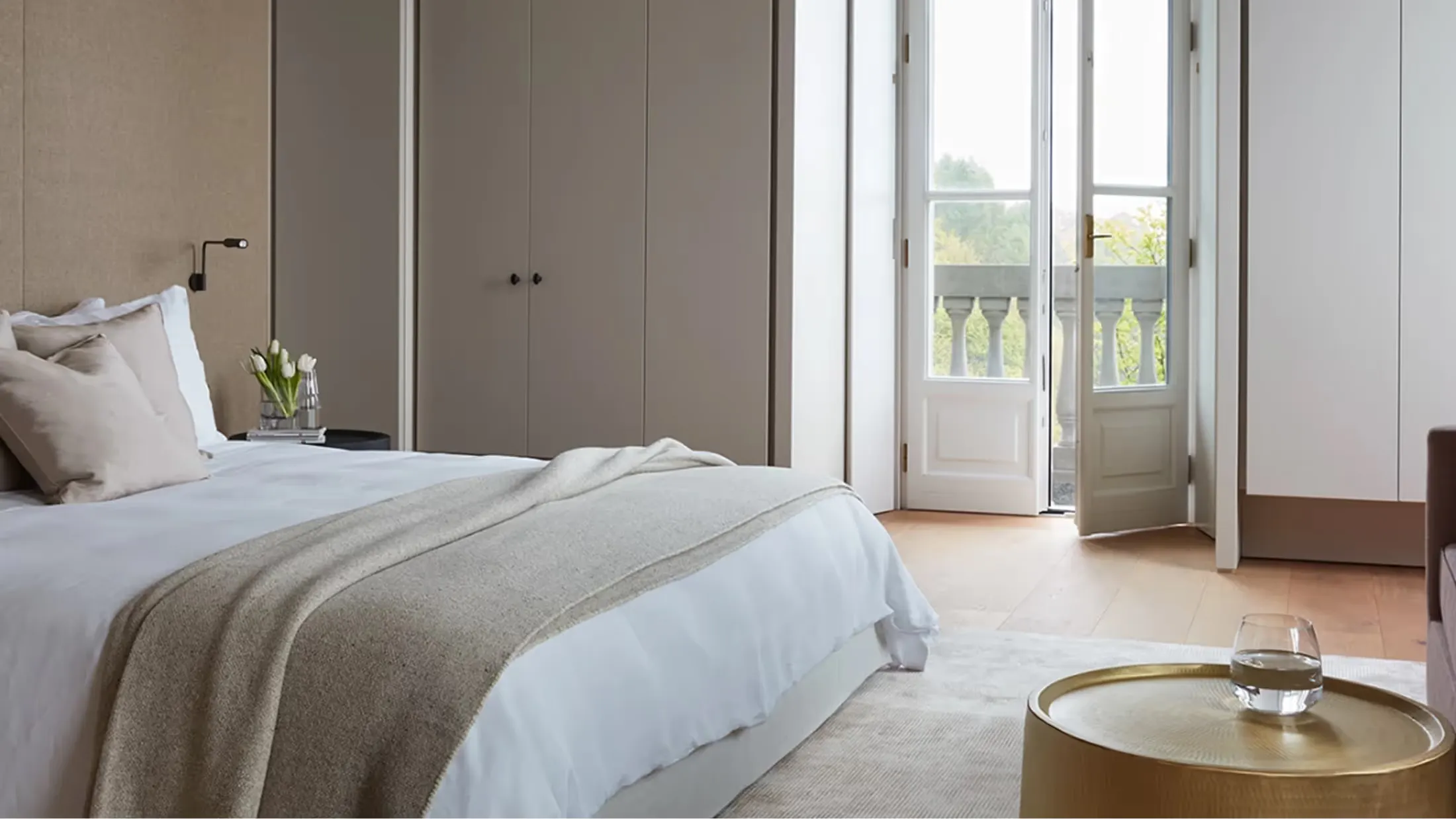 A bedroom with white bedding overlooking mountain peaks through wide terrace doors