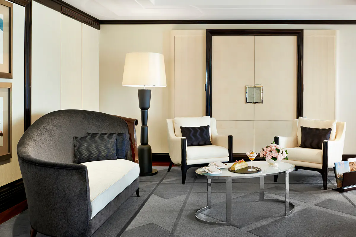 Suite sitting area with curved charcoal loveseat, cream chairs, and warm ambient lighting