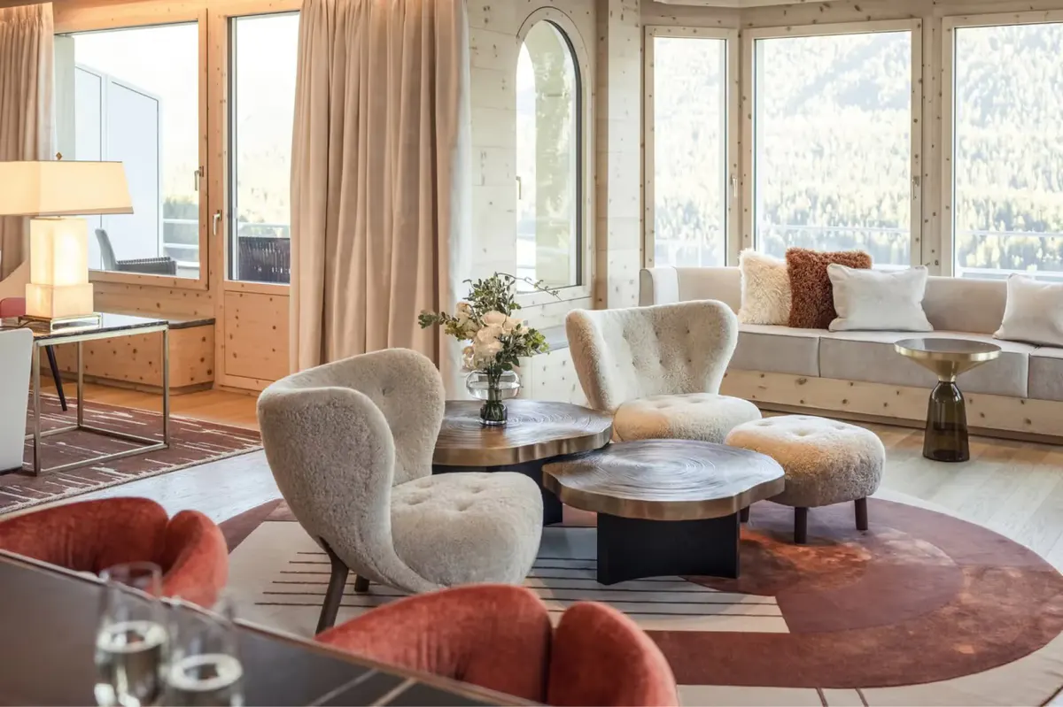 An interior suite with large windows framing Alpine peaks and morning light