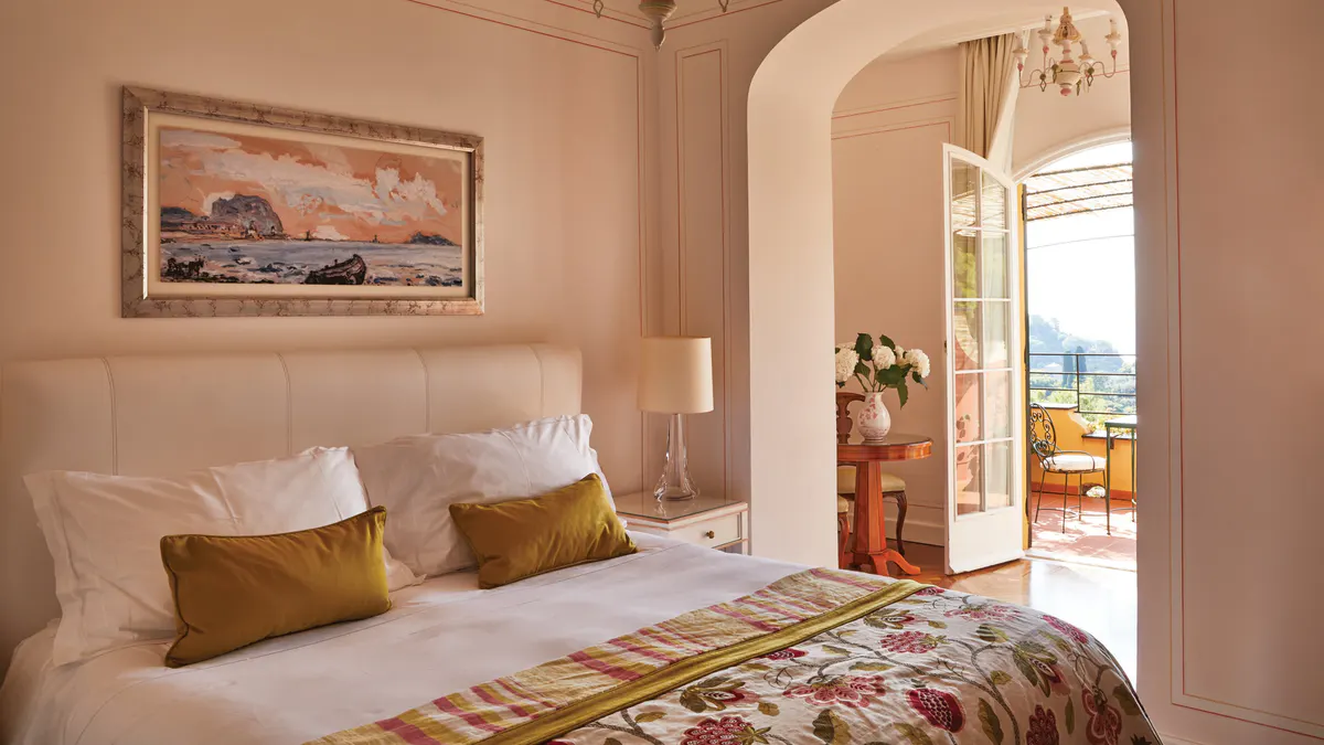 A bedroom nook with upholstered chair, framed botanical art, and cream tufted headboard