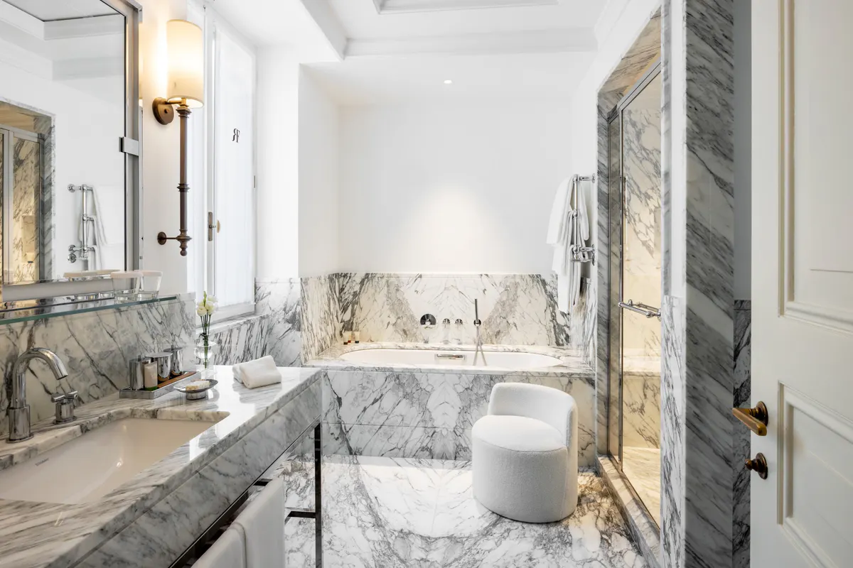 Marble bathroom with dual sinks, decorative panels, and white fixtures
