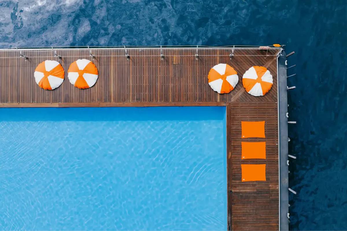 Pool edge with orange umbrellas and wooden deck overlooking water