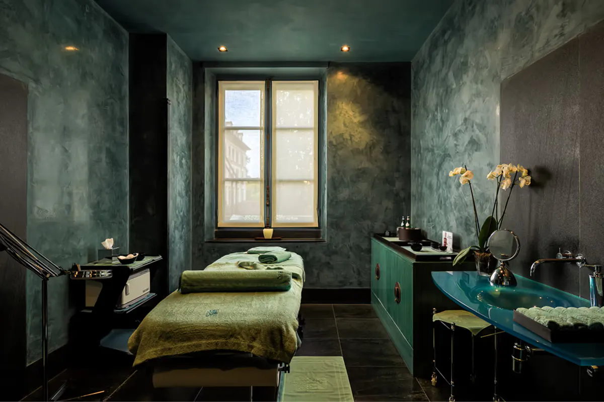 Spa treatment room with calming blue-green aesthetic and single massage bed