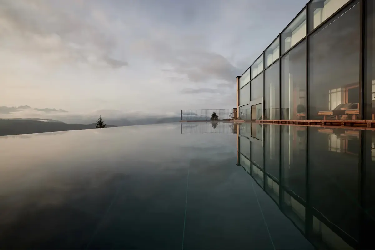 Infinity pool reflecting sky and mountains at dawn or dusk with misty atmosphere