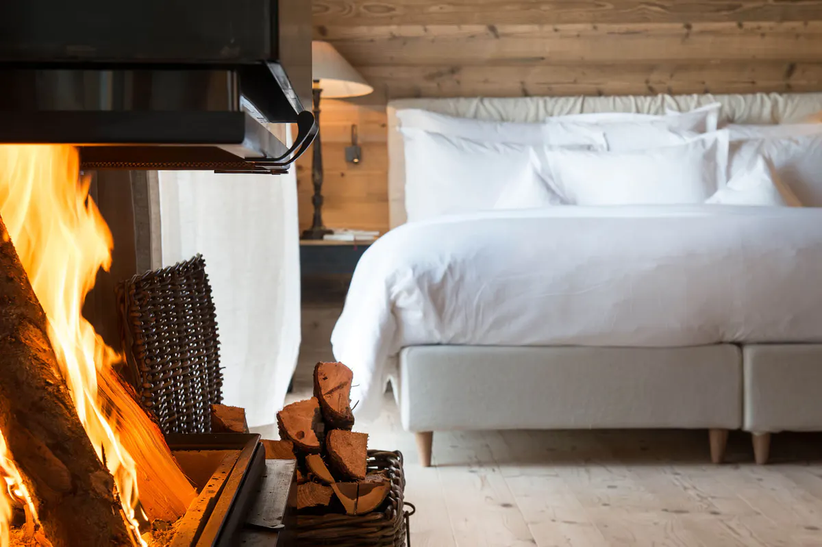 Fireplace with roaring flames beside a bed in a wooden room