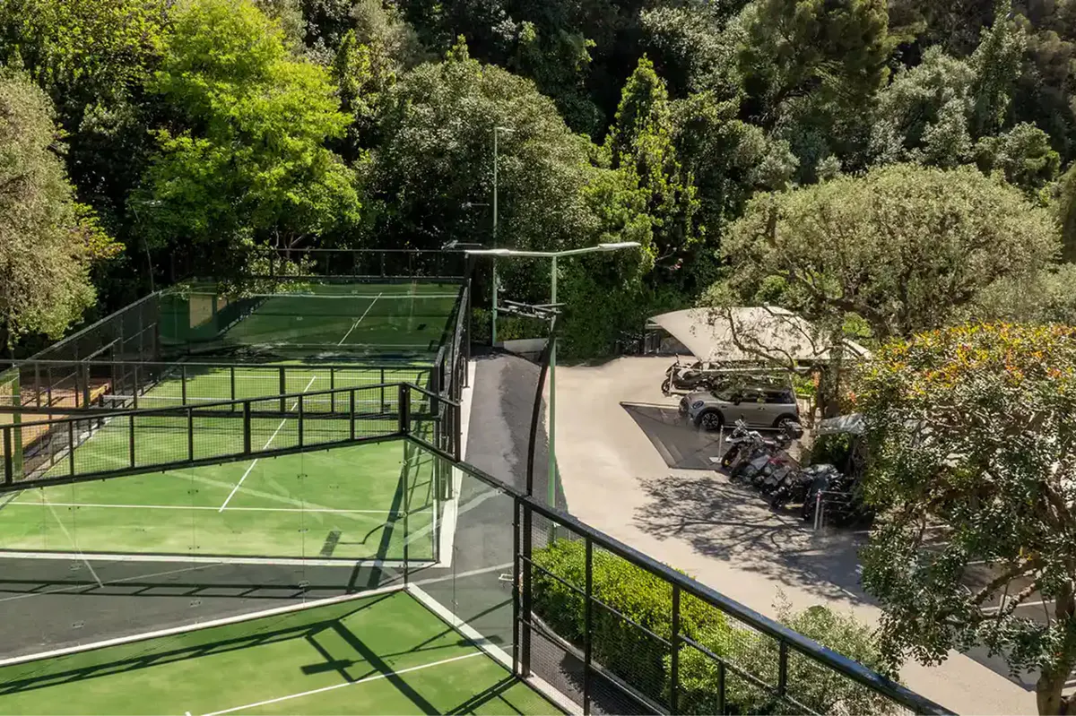 Outdoor tennis courts on hillside with green surfaces and perimeter fencing