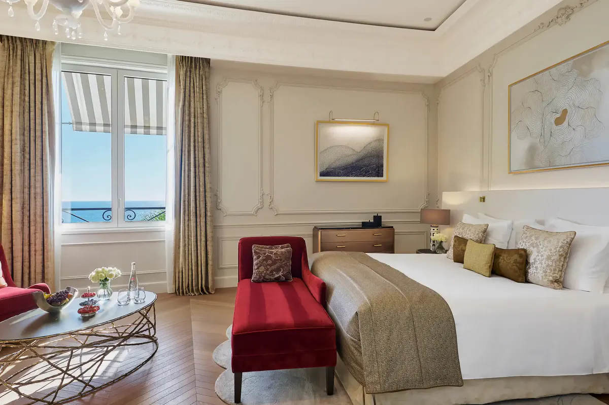 Bedroom with white bed and red accent bench at foot, sea view window