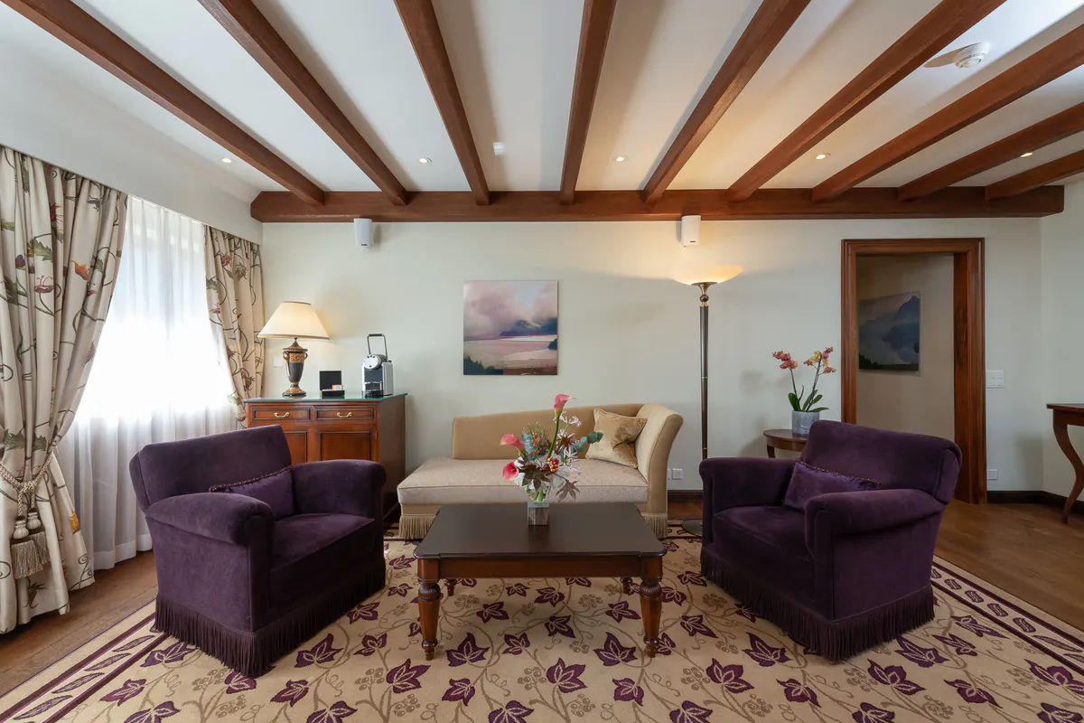A suite lounge with exposed timber framing, purple seating, artwork, and soft pendant lighting