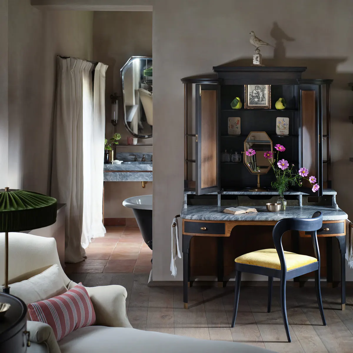 A bathroom with a black clawfoot tub, dark antique cabinetry, and a mirrored vanity nook