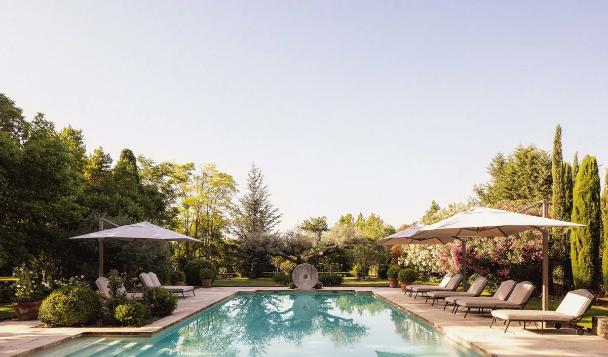 Heated saltwater pool with loungers and umbrellas surrounded by mature landscaping