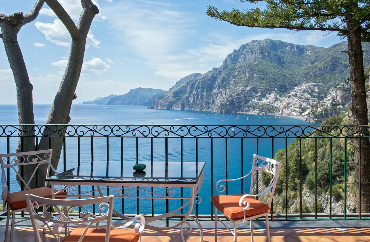 Furnished terrace with sea views through iron railing, lounge chairs with orange cushions, Mediterranean vista