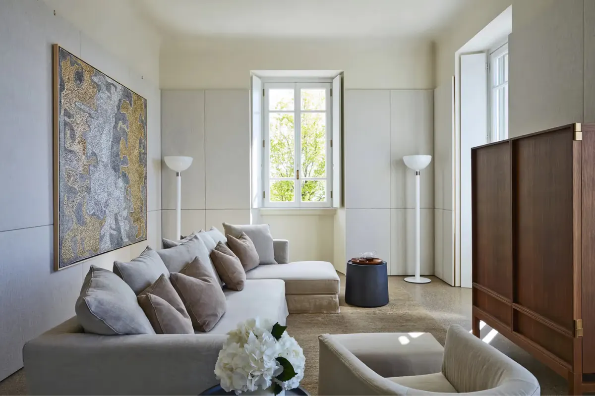 A living room with cream sofa, artwork, tall windows, and neutral tones