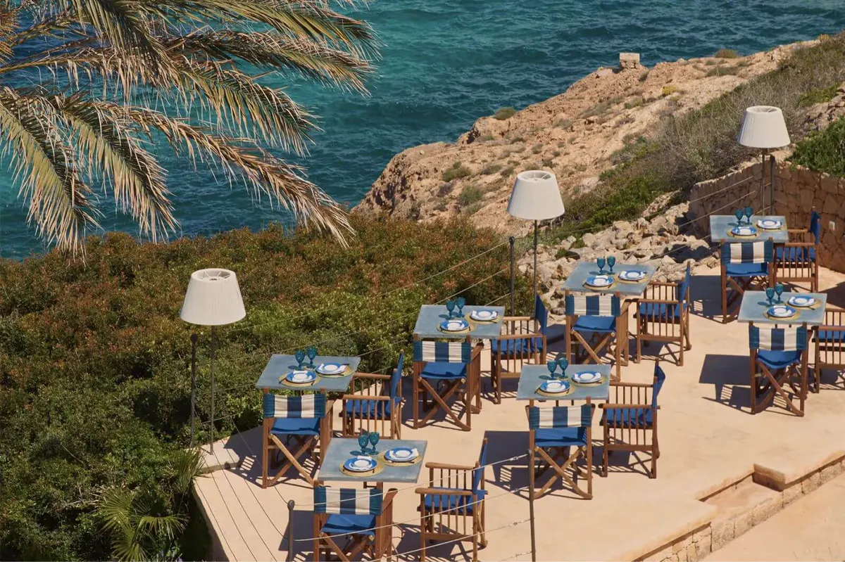 A beachside dining setup with wooden tables, purple accents, and panoramic seascapes